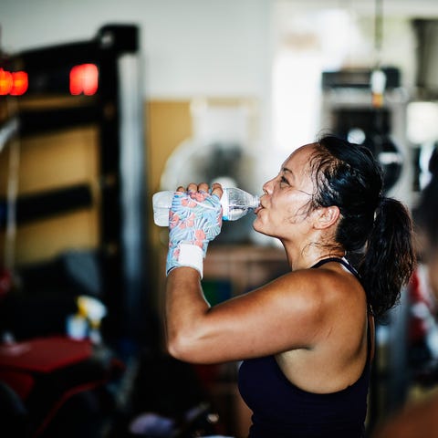 Sweating female boxer drinking water after workout in boxing gym