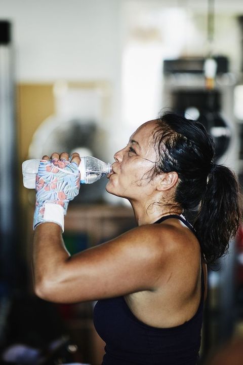 sweating female boxer drinking water after workout in boxing gym