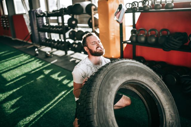 sweaty male athlete doing truck tire training in gym