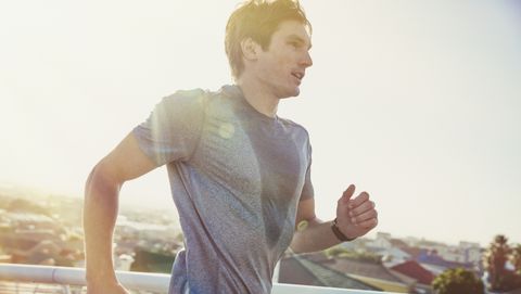 Sweaty male runner running on sunny urban footbridge at sunrise