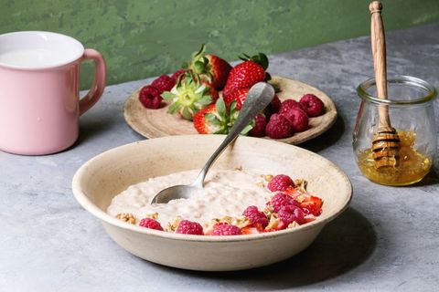 Sweet rice porridge pudding in ceramic plate with berries strawberry and raspberry, walnuts, honey and mug of milk on grey kitchen table with green wall as background