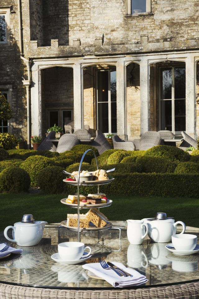 a table in a garden outside an old house with cake stand and a selection of cakes and sandwiches set for a traditional afternoon tea