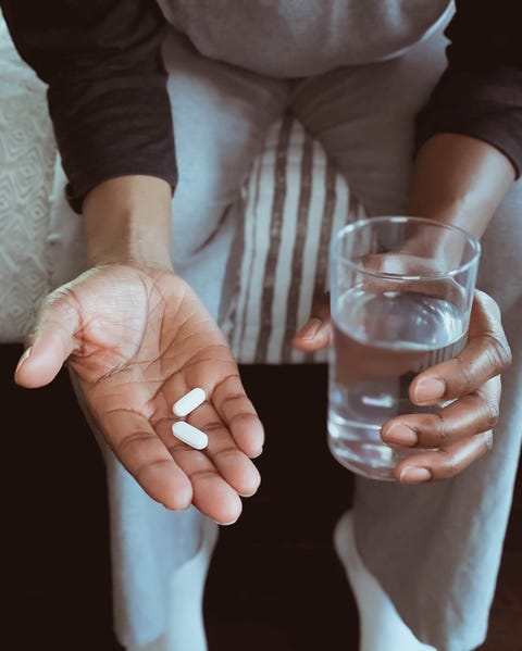 güneş yanığı için ibuprofen ev ilaçları alın Hap ve su tutan yatağın kenarında oturan kadının yakın çekim