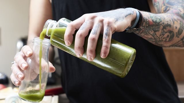 tattooed young man pouring in healthy smoothie in kitchen