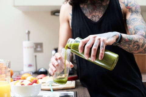 tattooed young man pouring in healthy smoothie in kitchen