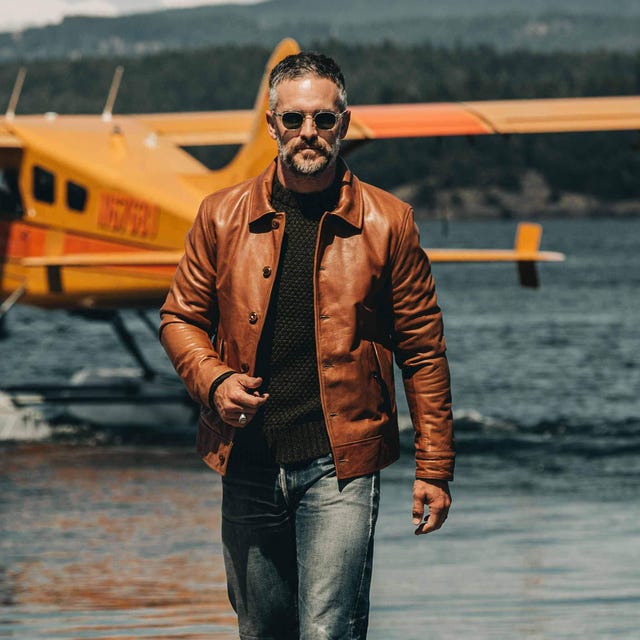 ma wearing leather jacket in front of a lake with a waterplane