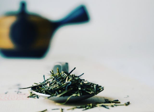 a close up of stems and leaves of kukicha karigane japanese green tea, a black and yellow kyusu teapot in the background