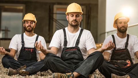 mannen met bouwhelmen doen aan meditatie op de bouwkavel