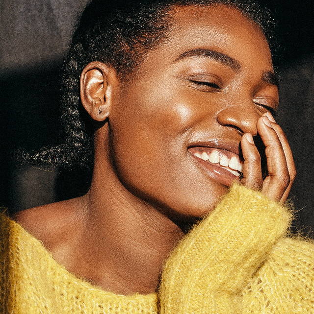 beautiful young black woman in yellow sweater covering mouth while laughing happily in bright sunlight
