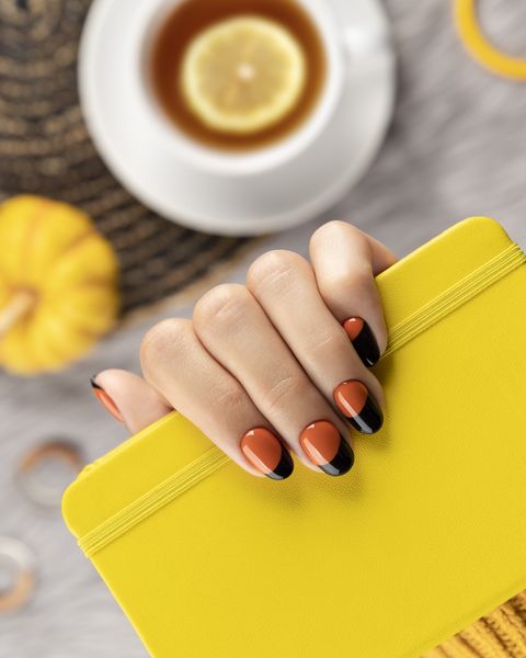 manicured womans hand holding yellow notepad on gray background trendy autumn halloween orange nail design