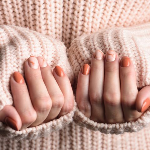 female hands with trendy autumn marble manicure in orange color pink knitted wool sweater