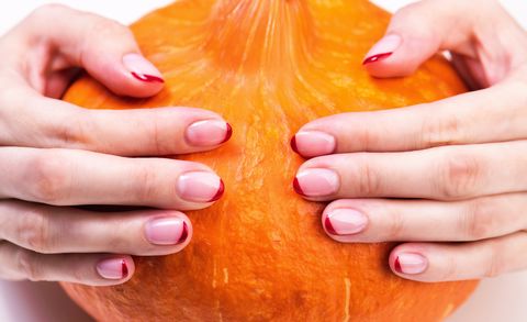 female hands with a trendy autumn french manicure with red tips at the free edge of the nail orange pumpkin on white background orange squash for thanksgiving or halloween