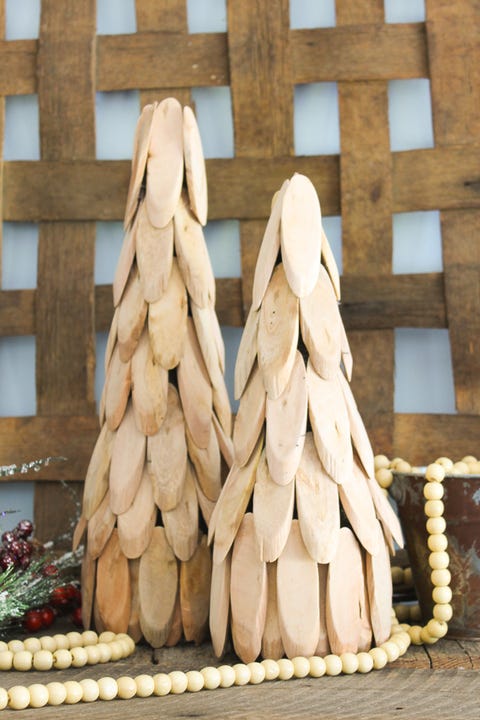 two tabletop sized decorative christmas trees made of wood slices, there are wooden beads around them and they are in front of a piece of wood lattice