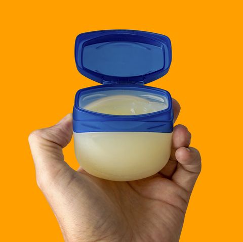 the left hand of a young female person holds a container with skincare cream over colored clean background