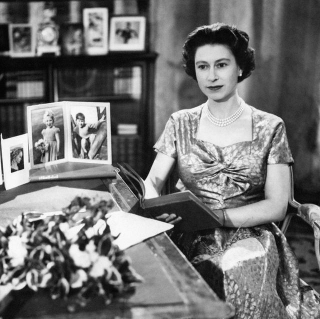 first televised queen's speech on christmas from sandringham, queen elizabeth sits reading a book in a silk dress with family photos on her desk