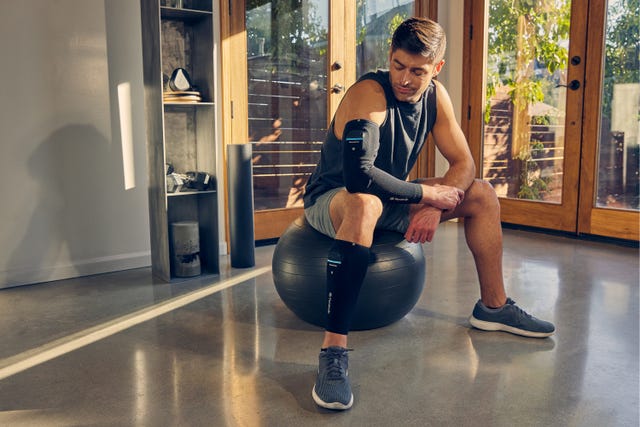 a man sitting on an exercise ball wearing the therabody recoverypulse collection