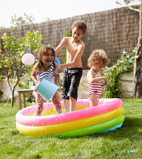 three young children play in a small pink, yellow, and green inflatable pool in the backyard, a summer activity you can do at home