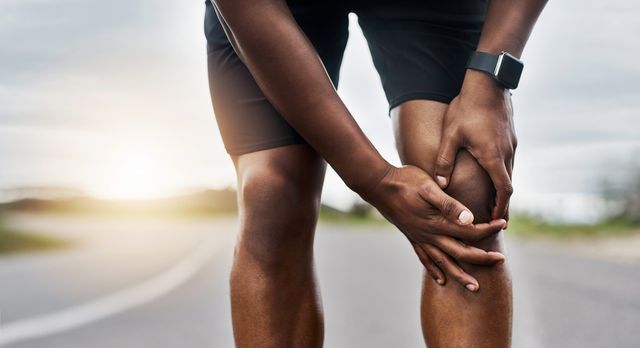 male runner holds knee after twisting it on a run