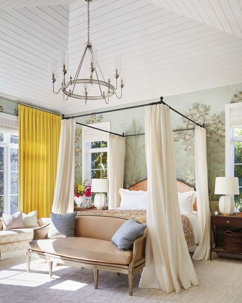 linen panels drape an iron and walnut bed and there are yellow curtains on the windows