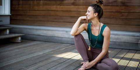 thoughtful smiling woman looking away while sitting on hardwood floor against house