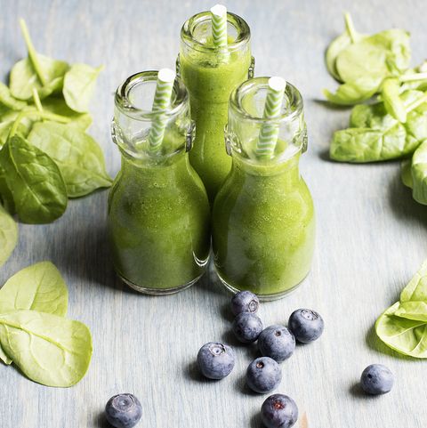 Three bottles of fresh green smoothies with spinach and blueberries
