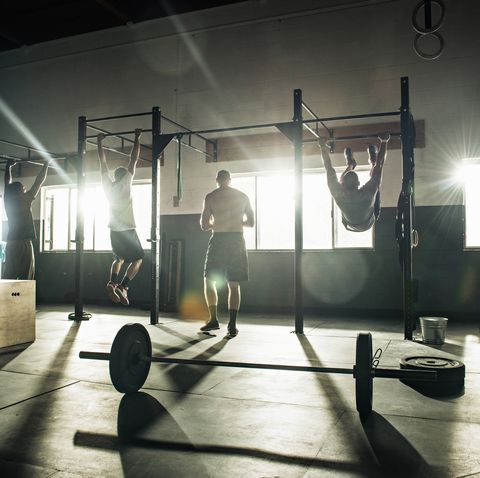 Three men training on exercise bar in gymnasium