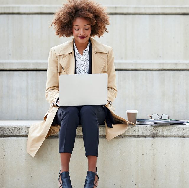 vrouw met afro zit met laptop op schoot op betonnen traptreden te werken