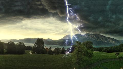 bliksemschicht slaat in boom bij groen grasland in bergen met meer op de achtergrond