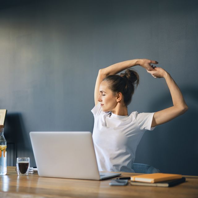 tired businesswoman stretching arms while sitting at desk in home office