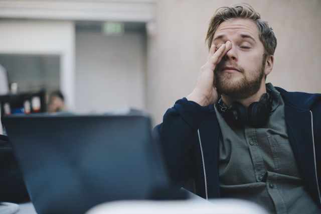 tired computer programmer rubbing eyes while sitting in office