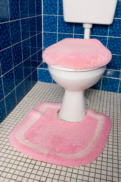 A toilet with fluffy pink seat cover and rug