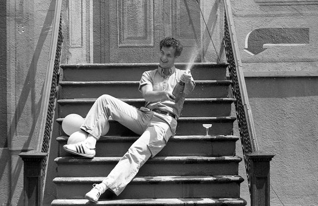 tom hanks, durante el rodaje de la película 'despedida de soltero' el actor está sentado en unas escaleras, riendo mientras descorcha una botella de champán y el corcho sale disparado
