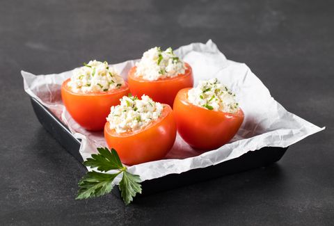 Tomatoes stuffed with parsley and cottage cheese on a serving plate on a dark gray background