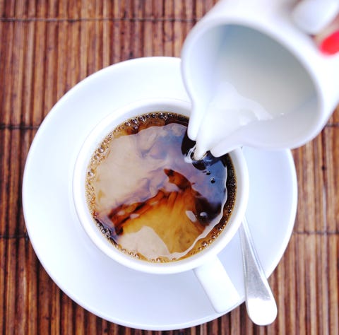 Top of view of pouring stream milk into a cup of espresso on a wooden table.