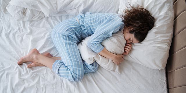 top view of depressed woman in pajamas lying in bed in bedroom