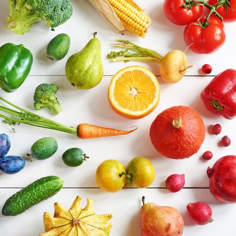Top view of rainbow colored fruits and vegetables on a white table.