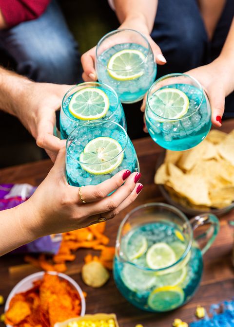 four hands cheersing with a blue cocktail garnished with a lemon slice