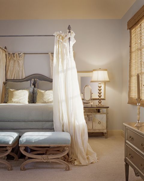 bedroom decorated in traditional style with metal four poster bed with gauzy drapes hanging down from it and stools with pale blue cushions at the end of it