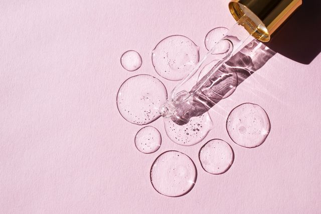 transparent drops of hyaluronic acid and glass pipette on pink background