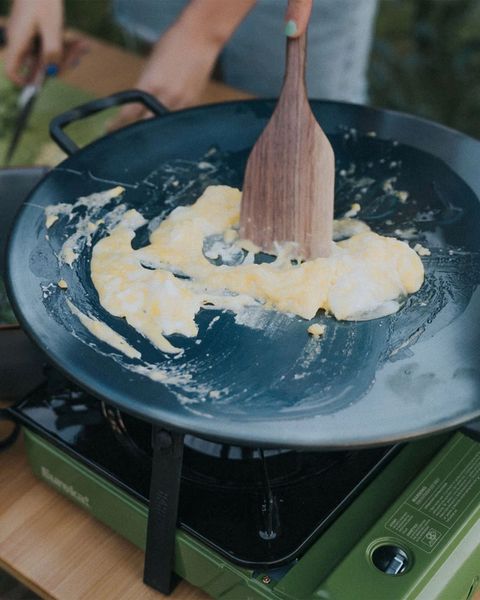 a person making scrabbled eggs in a wok on a camp stove