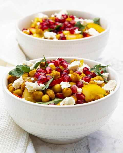 two bowls of vegetarian salad with chickpeas turmeric bell peppers tomatoes parsley feta cheese and pomegranate seeds