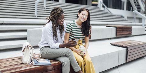 two female college students having a laugh while watching something on the smartphone