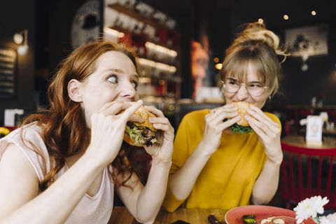 two female friends eating burger in a restaurant