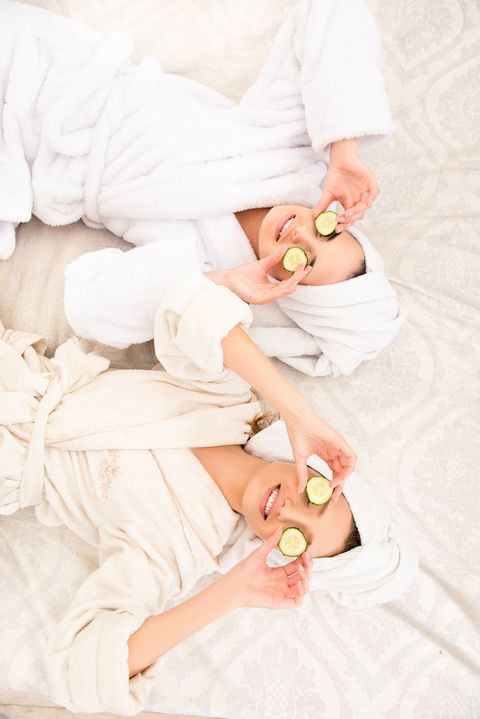 two funny young women with cucumbers on eyes and towel on their heads lying on the bed
