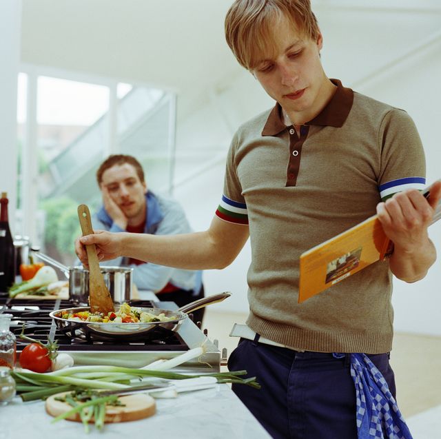 two men in kitchen, one preparing vegetables in frying pan