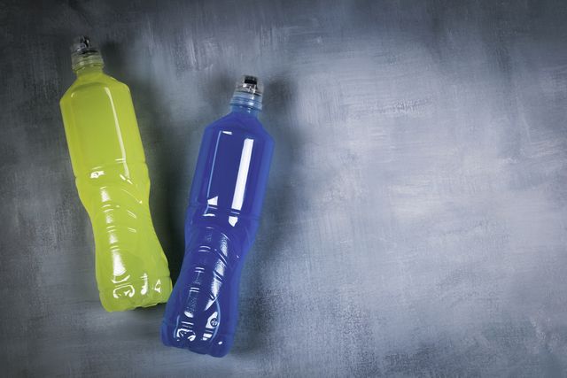 two plastic bottles with isotonic energy blue and yellow transparent sport drink on gray background top view, copy space