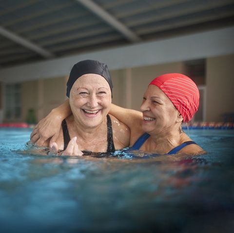 two senior women embracing together in swimming indoor pool