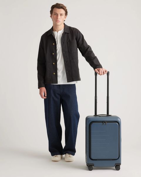 a man holding a quince front pocket carry on hard shell suitcase