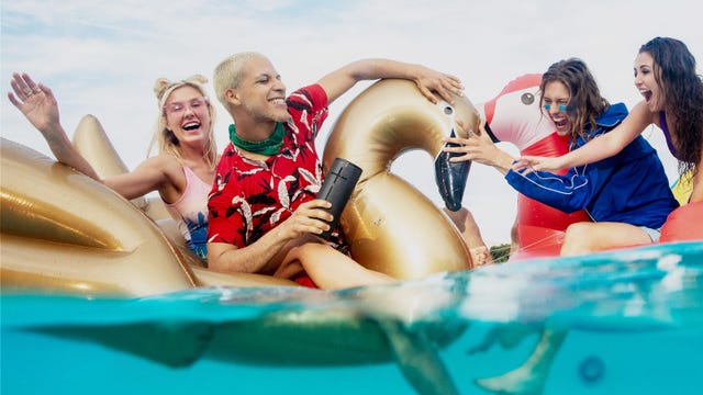 man riding golden swan pool floaty with ultimate ears megaboom 3 waterproof speaker in hand surrounded by three women