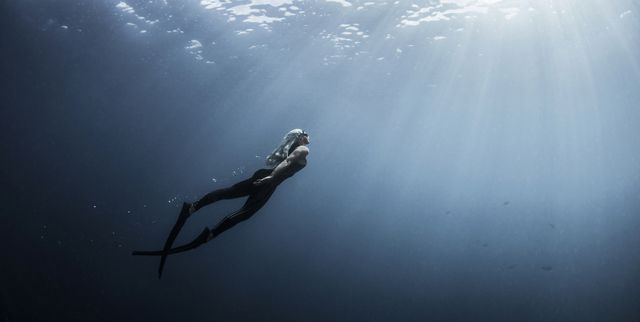 underwater view of female free diver moving up towards sun rays, new providence, bahamas